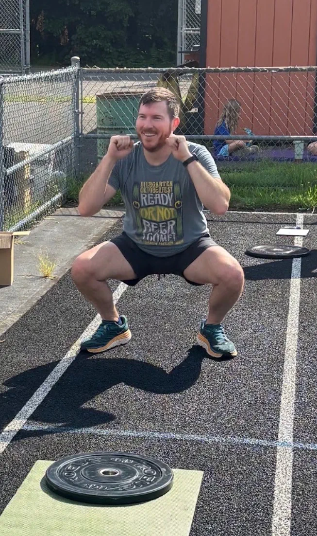 A community-workout participant holding a squat beside training equipment